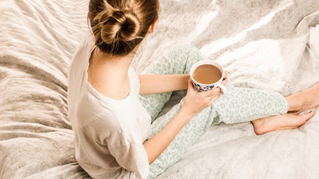 A woman holding a cup of tea on a silk bed