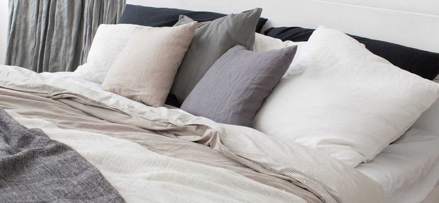 Bed with white and grey linens and a lot of pillows.