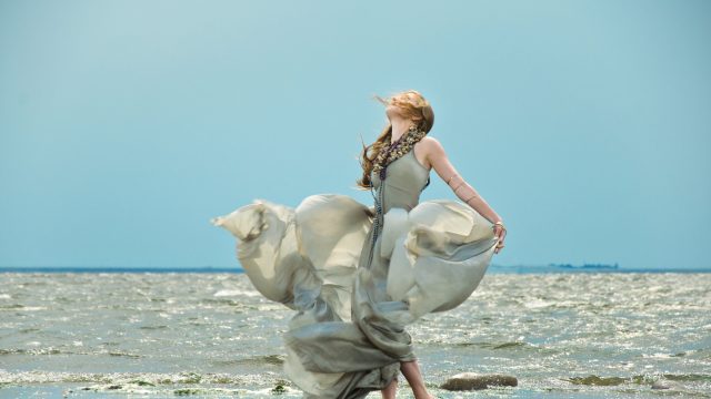 A woman dances in a silk dress on a beach